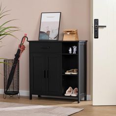 a black cabinet sitting next to a door with shoes on top of it and an umbrella in the corner