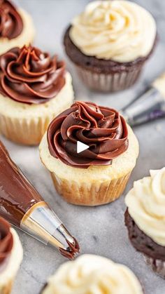 chocolate cupcakes with white frosting on a baking sheet next to a pastry knife