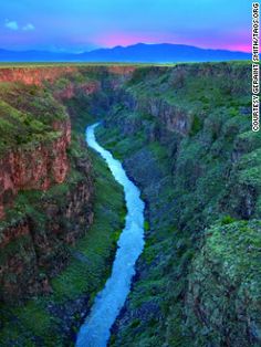 a river flowing through a canyon surrounded by lush green grass and mountains in the distance