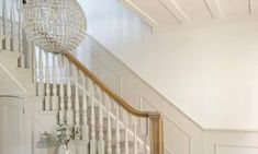 a white staircase with chandelier and vases on the floor next to it