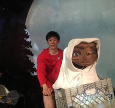 a man sitting next to a statue of an alien in a red shirt and white hoodie