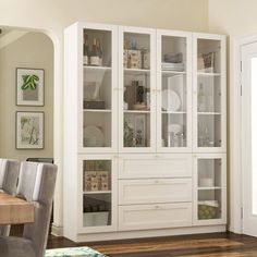 a white cabinet with glass doors and drawers in a living room area next to a dining room table