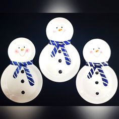 three snowmen made out of white plates on a black surface