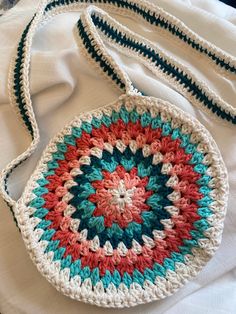 a crocheted bag sitting on top of a white bed next to a pillow