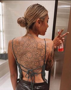 a woman with a tattoo on her back pointing at something in front of the mirror