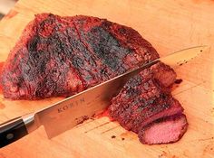 a large piece of meat sitting on top of a cutting board next to a knife