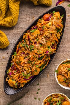 two bowls filled with noodles and vegetables on top of a wooden table next to other dishes