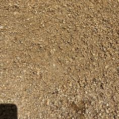 the shadow of a person standing in front of a dirt field with rocks on it