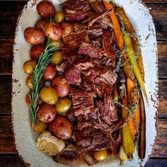 a plate full of roast, potatoes and carrots on a white platter with rosemary sprigs