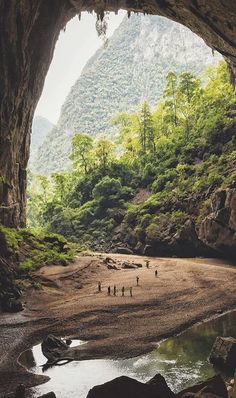 some people are standing in the middle of a cave with trees and mountains behind them