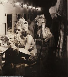 an old photo of two women dressed in costumes sitting at a desk and one is holding a phone