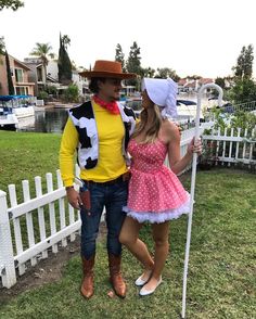 a man and woman dressed up in costumes standing next to each other near a white picket fence