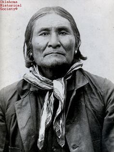 an old black and white photo of a native american man with long hair wearing a scarf