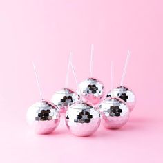 four shiny silver balls with sticks sticking out of them on a pink background, one is empty