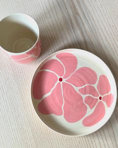 a pink and white plate with flowers on it next to a cup of tea or water