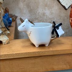 a white cow shaped bowl sitting on top of a wooden table next to a vase