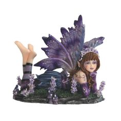 a purple fairy figurine sitting on top of a lush green field with flowers