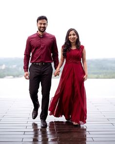 a man and woman holding hands while walking down a walkway in front of a body of water