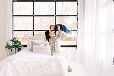 a woman laying on top of a white bed next to a window with lots of windows