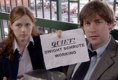 a man and woman holding up a sign that says quiet, wright schrute working