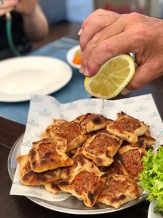 a person holding a lemon slice over some food on a plate with other plates and utensils