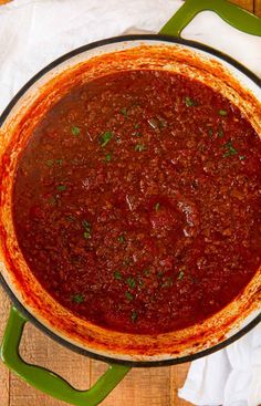 a large pot filled with chili sauce on top of a wooden table next to a napkin