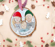 a christmas ornament with two people and a baby on it, surrounded by pine branches