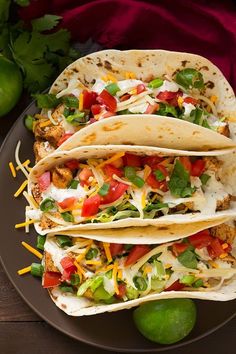 three tacos on a plate with limes and cilantro