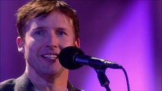 a man standing next to a microphone in front of a purple background and wearing a suit