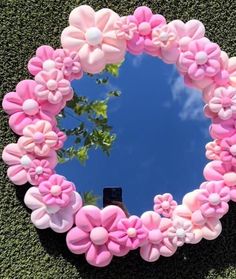 a mirror with pink flowers in the shape of a heart on top of green grass