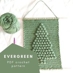 a green crochet christmas tree is next to a ball of yarn and a knitting needle