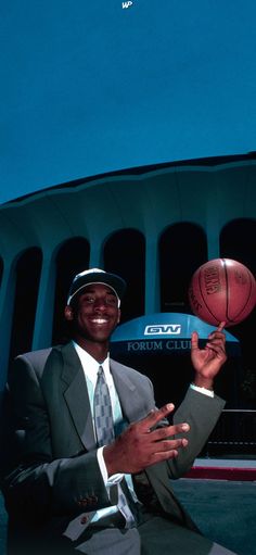 a man in a suit and tie holding a basketball near a building with a sky background