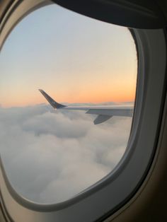 an airplane window looking out at the clouds below it and in the distance, there is a plane wing