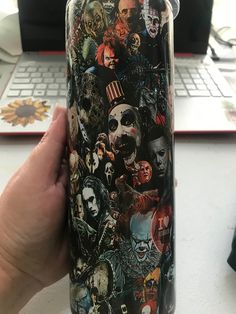 a hand holding a tumbler cup with many different pictures on it and a keyboard in the background