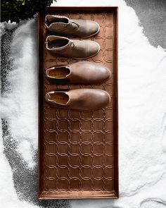 four pairs of shoes are lined up on a brown shoe tray with white powder in the background