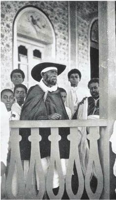 an old black and white photo of a man in a hat standing on a balcony