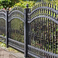 an iron fence is shown in front of some bushes and flowers on the side walk