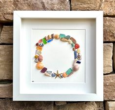 a white frame holding a colorful beaded bracelet with shells and starfish on it