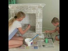 two children are sitting on the floor painting a brick fireplace