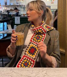 a woman holding a drink in her right hand and wearing a scarf around her neck