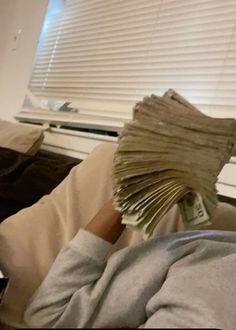 a person laying in bed under a window with money coming out of their hands and covering his face