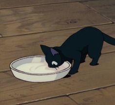 a black cat eating out of a white bowl on the floor with it's mouth open