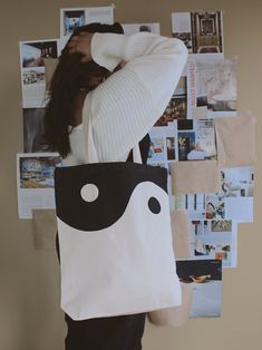 a woman holding a black and white tote bag in front of a wall covered with pictures