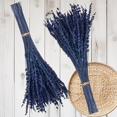 two bundles of dried lavender sitting next to a basket on a white wooden table top