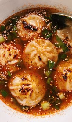 a white bowl filled with dumplings covered in broth and sesame seed sprinkles