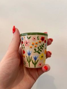 a woman's hand holding a cup with flowers painted on the inside and outside