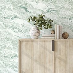 a white vase sitting on top of a wooden cabinet next to a wallpapered wall