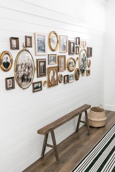 a wooden bench sitting in front of a white wall with pictures hanging on the wall