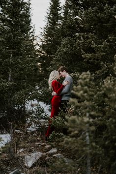 an engaged couple cuddles in the snow surrounded by evergreen trees at their engagement session