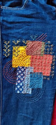 a pair of blue jeans with colorful patches on them and some red material in the back pocket